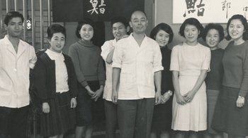 Movie still from “Jiro Dreams of Sushi” (2011), directed by David Gelb – An old black and white photo of a group of people; Medium shot, Low angle