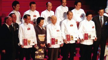 Movie still from “Jiro Dreams of Sushi” (2011), directed by David Gelb – A group of people standing next to each other on a stage; Wide shot, High angle