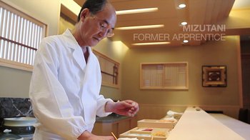 Movie still from “Jiro Dreams of Sushi” (2011), directed by David Gelb – A man in a white lab coat is working at a counter; Medium shot, Low angle