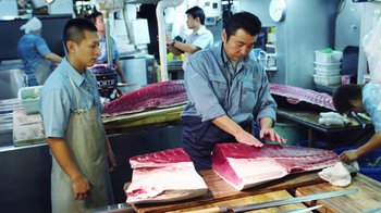 Movie still from “Jiro Dreams of Sushi” (2011), directed by David Gelb – A man cutting a piece of meat on top of a cutting board; Medium shot, Overhead angle