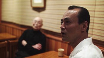 Movie still from “Jiro Dreams of Sushi” (2011), directed by David Gelb – Two men sitting at a table in front of a wooden wall; Close Up shot, Low angle