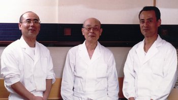 Movie still from “Jiro Dreams of Sushi” (2011), directed by David Gelb – A group of men standing next to each other in a room; Medium shot, Low angle
