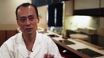 Movie still from “Jiro Dreams of Sushi” (2011), directed by David Gelb – A man sitting in front of a counter in front of a sink; Close Up shot, Low angle