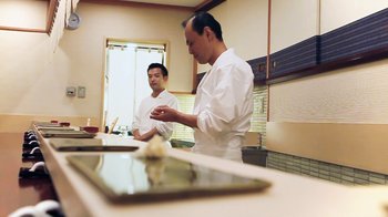 Movie still from “Jiro Dreams of Sushi” (2011), directed by David Gelb – Two men in white chef's uniforms in a kitchen; Medium shot, Low angle