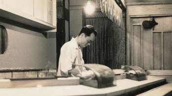 Movie still from “Jiro Dreams of Sushi” (2011), directed by David Gelb – A man in an apron cutting a loaf of bread; Medium shot, High angle