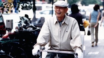 Movie still from “Jiro Dreams of Sushi” (2011), directed by David Gelb – An older man riding a bike down a street; Close Up shot, Low angle