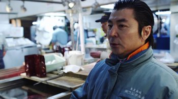 Movie still from “Jiro Dreams of Sushi” (2011), directed by David Gelb – A man standing in front of a counter in a kitchen; Medium shot, Over the shoulder angle