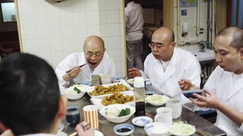 Movie still from “Jiro Dreams of Sushi” (2011), directed by David Gelb – Two men sitting at a dinner table eating food; Medium shot, Over the shoulder angle