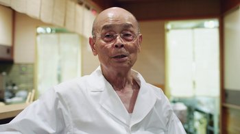 Movie still from “Jiro Dreams of Sushi” (2011), directed by David Gelb – An older man wearing glasses and a white shirt; Medium shot, Low angle
