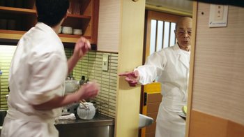 Movie still from “Jiro Dreams of Sushi” (2011), directed by David Gelb – A man in a chef's outfit pointing at something; Medium shot, Over the shoulder angle