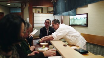 Movie still from “Jiro Dreams of Sushi” (2011), directed by David Gelb – A group of people sitting at a table with plates of food on it; Medium shot, High angle