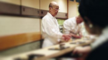 Movie still from “Jiro Dreams of Sushi” (2011), directed by David Gelb – Two men in a kitchen preparing food for a meal; Medium shot, Over the shoulder angle