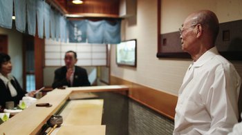 Movie still from “Jiro Dreams of Sushi” (2011), directed by David Gelb – Two people in a restaurant talking to each other; Medium shot, Over the shoulder angle