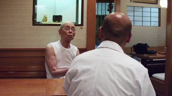 Movie still from “Jiro Dreams of Sushi” (2011), directed by David Gelb – An older man sitting in front of a mirror; Medium shot, Over the shoulder angle