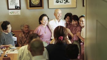 Movie still from “Jiro Dreams of Sushi” (2011), directed by David Gelb – A group of people standing in front of a camera; Medium shot, Over the shoulder angle