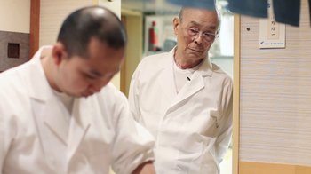 Movie still from “Jiro Dreams of Sushi” (2011), directed by David Gelb – An older man looking at himself in the mirror; Medium shot, Over the shoulder angle