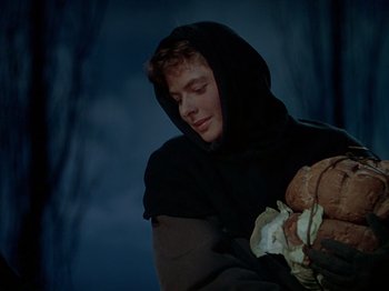 Movie still from “Joan of Arc” (1948), directed by Victor Fleming – A young man in a hooded cloak holding a bunch of food; Close Up shot, Low angle