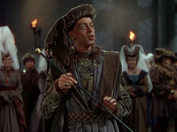 Movie still from “Joan of Arc” (1948), directed by Victor Fleming – A man in a costume holding a spear and a hat; Medium shot, Over the shoulder angle