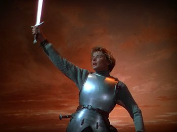 Movie still from “Joan of Arc” (1948), directed by Victor Fleming – A woman dressed as joan of arc holding a sword in front of a red sky; Medium shot, Low angle