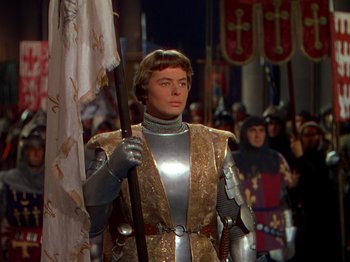 Movie still from “Joan of Arc” (1948), directed by Victor Fleming – A man dressed as a medieval knight holding a flag; Medium shot, High angle