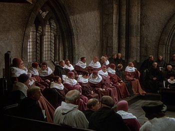 Movie still from “Joan of Arc” (1948), directed by Victor Fleming – A group of people sitting on pedestals in a church; Wide shot, High angle