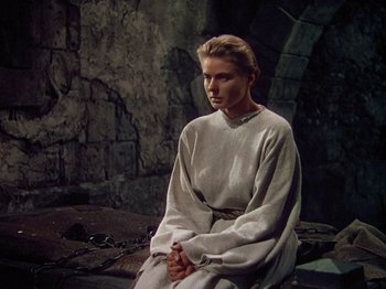 Movie still from “Joan of Arc” (1948), directed by Victor Fleming – A woman sitting on the ground wearing a white robe; Medium shot, High angle