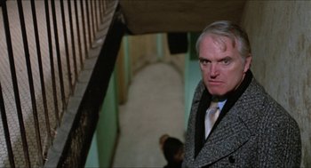 Movie still from “Joe” (1970), directed by John G. Avildsen – A man in a suit and tie standing in a hallway; Close Up shot, Over the shoulder angle