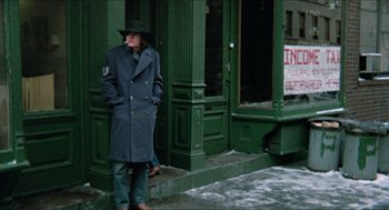 Movie still from “Joe” (1970), directed by John G. Avildsen – A man standing on the side of the street smoking a cigarette in front of a building; Wide shot, Low angle