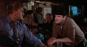 Movie still from “Joe” (1970), directed by John G. Avildsen – Two men sitting at a table in front of each other at a bar; Medium shot, Over the shoulder angle