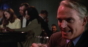 Movie still from “Joe” (1970), directed by John G. Avildsen – A man sitting in front of a group of people; Close Up shot, Over the shoulder angle