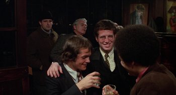 Movie still from “Joe” (1970), directed by John G. Avildsen – A group of men standing around each other at a party; Medium shot, Over the shoulder angle