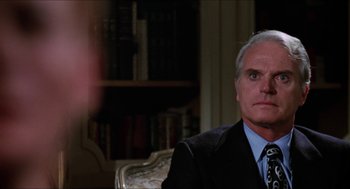Movie still from “Joe” (1970), directed by John G. Avildsen – An older man wearing a suit and tie in front of a bookshelf; Close Up shot, Over the shoulder angle