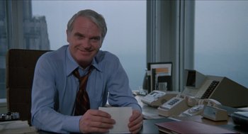 Movie still from “Joe” (1970), directed by John G. Avildsen – A man sitting at a desk holding a coffee cup; Medium shot, Low angle