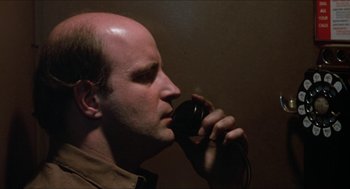 Movie still from “Joe” (1970), directed by John G. Avildsen – A man with a bald head talking on a phone; Close Up shot, Low angle
