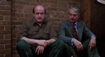 Movie still from “Joe” (1970), directed by John G. Avildsen – Two men sitting next to each other in front of a brick wall; Medium shot, Low angle