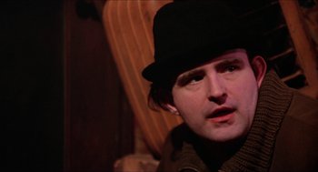 Movie still from “Joe” (1970), directed by John G. Avildsen – A man wearing a black hat sitting in front of a wooden chair; Close Up shot, Over the shoulder angle