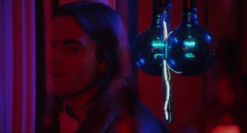 Movie still from “Joe” (1970), directed by John G. Avildsen – A man with long hair standing next to a chandelier; Close Up shot, Over the shoulder angle