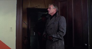 Movie still from “Joe” (1970), directed by John G. Avildsen – A man in a gray coat holding a black cane; Medium shot, Low angle