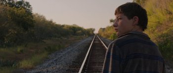 Movie still from “Joe” (2013), directed by David Gordon Green – A young boy standing on a train track; Medium shot, Over the shoulder angle