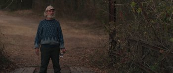 Movie still from “Joe” (2013), directed by David Gordon Green – An older man walking down a path holding a beer; Medium shot, Over the shoulder angle