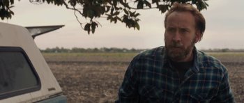Movie still from “Joe” (2013), directed by David Gordon Green – A man in a plaid shirt sitting in a field; Close Up shot, Over the shoulder angle