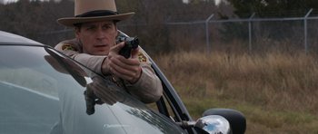 Movie still from “Joe” (2013), directed by David Gordon Green – A police officer holding a gun in a car; Medium shot, Over the shoulder angle