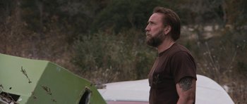 Movie still from “Joe” (2013), directed by David Gordon Green – A man standing next to a green object; Close Up shot, Over the shoulder angle