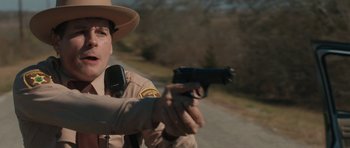 Movie still from “Joe” (2013), directed by David Gordon Green – A police officer is holding a gun and pointing it; Close Up shot, Over the shoulder angle