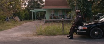 Movie still from “Joe” (2013), directed by David Gordon Green – A man sitting on the side of the road in front of a house; Wide shot, Over the shoulder angle