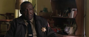 Movie still from “Joe” (2013), directed by David Gordon Green – A police officer sitting at a desk in a room; Close Up shot, Over the shoulder angle