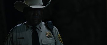 Movie still from “Joe” (2013), directed by David Gordon Green – A man in a sheriff's uniform is wearing a badge; Close Up shot, Over the shoulder angle