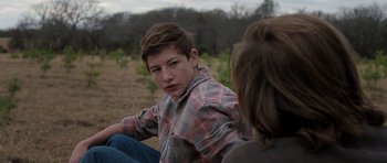 Movie still from “Joe” (2013), directed by David Gordon Green – A young man sitting on the ground with another person; Close Up shot, Over the shoulder angle
