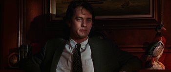 Movie still from “Joe Versus the Volcano” (1990), directed by John Patrick Shanley – A man wearing a suit and tie sitting in a chair; Close Up shot, Low angle
