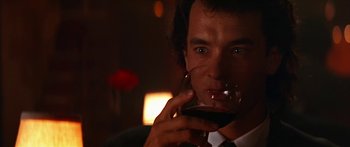 Movie still from “Joe Versus the Volcano” (1990), directed by John Patrick Shanley – A person holding a glass of red wine; Close Up shot, Low angle